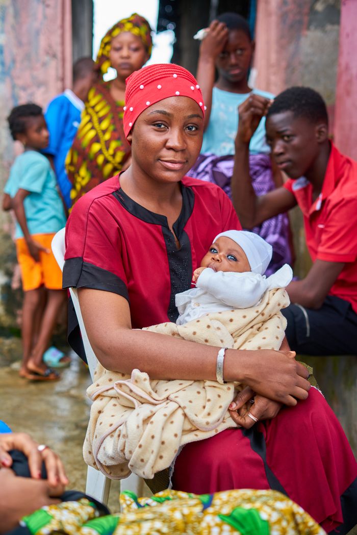 A mother in traditional attire cradling her infant, surrounded by family members outside.