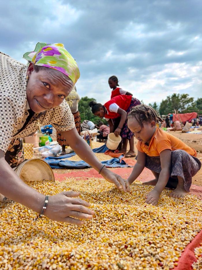 Women and child sorting corn kernels on an outdoor market.