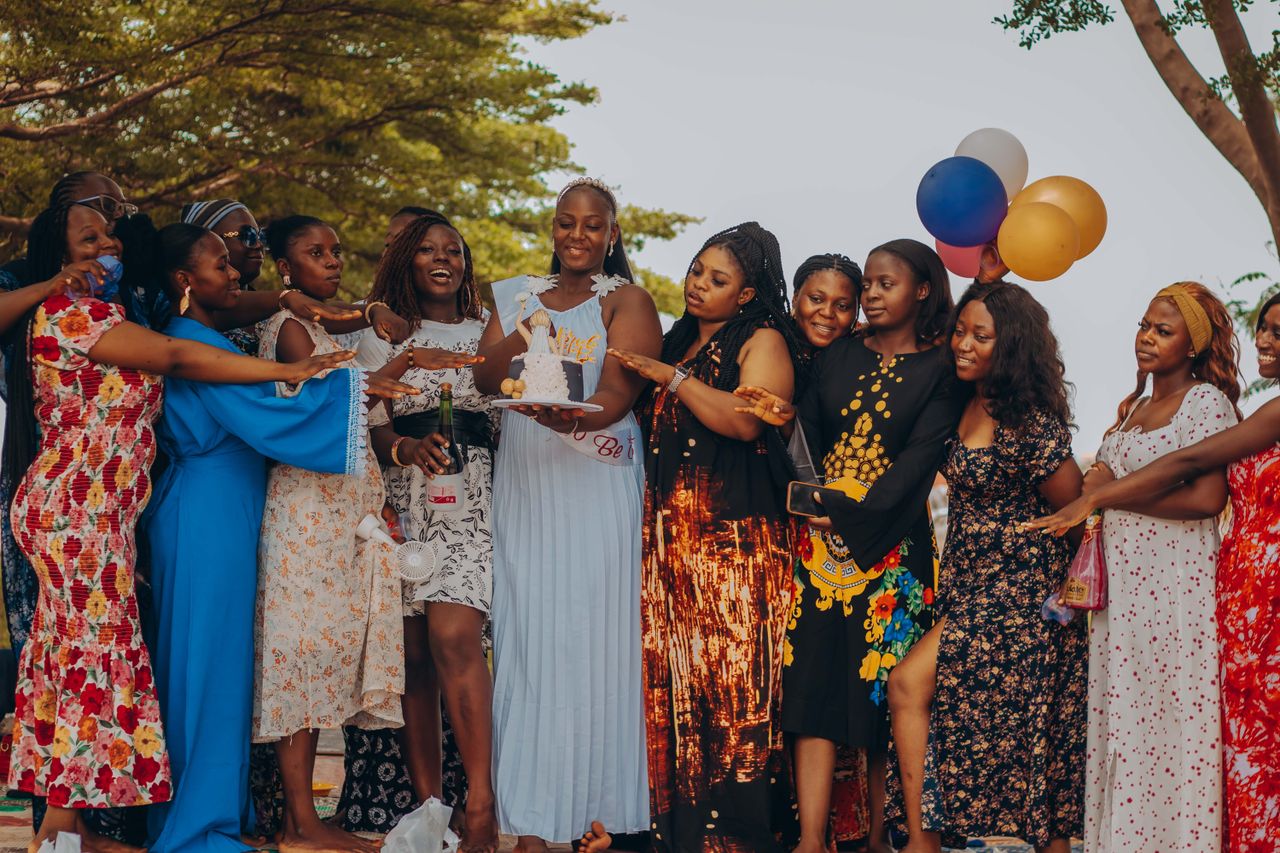 Home A joyful bridal shower with women celebrating outdoors, holding balloons and a cake.